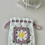 Pochette fleur au crochet blanche avec marguerite mauve, jaune et verte et fermeture par cordons