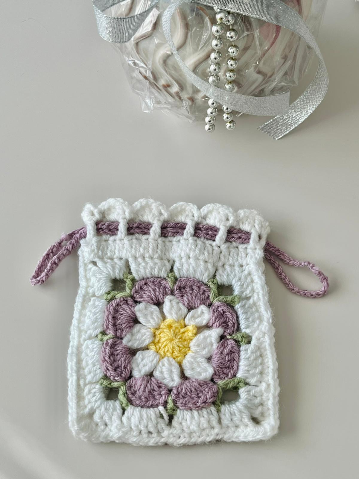 Pochette fleur au crochet Marguerite Pochette fleur au crochet blanche avec marguerite mauve, jaune et verte et fermeture par cordons